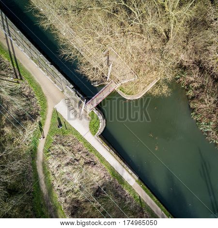 Vertical drone view of an English canal scene with lock and towpath in view surrounded by winter trees on a bright February day.