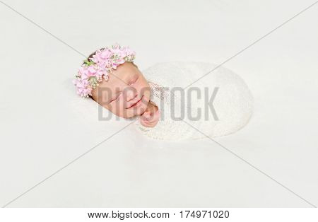 cute newborn baby swaddled in white diaper smiling asleep with flowers on headband