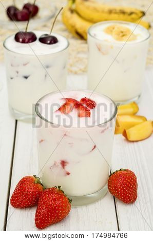 Strawberry, banana and cherry yoghurt on a white wooden background. Healthy diet