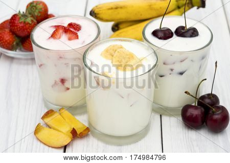 Strawberry, banana and cherry yoghurt on a white wooden background. Healthy diet