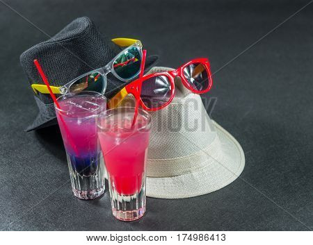 Two colored drinks a combination of dark blue with purple the second combination of red with pink long drink glass yellow and red sunglasses white and black hats party set