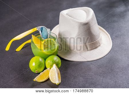 colored drink a combination of blue and green decorated with lemon and melon a glass a piece of lemon and two limes yellow sunglasses white hat party set