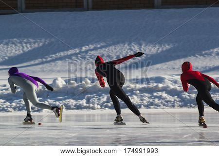 Speed skating competition on ice rink at winter sunny day - children's sport concept, telephoto
