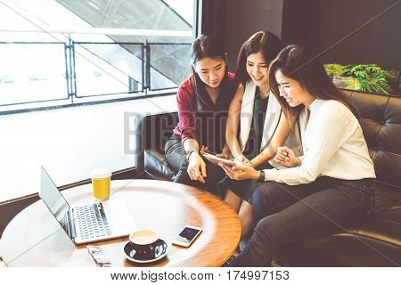Three beautiful Asian girls using smartphone and laptop chatting on sofa at cafe modern lifestyle with gadget technology or working woman on casual business concept