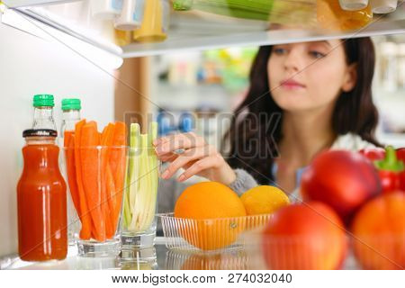 Portrait Of Female Standing Near Open Fridge Full Of Healthy Food, Vegetables And Fruits. Portrait O