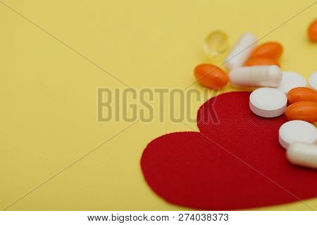 Red Heart And A Lot Of Bright Pills Of Drugs On A Yellow Background. Cropped Shot, Horizontal, Side 