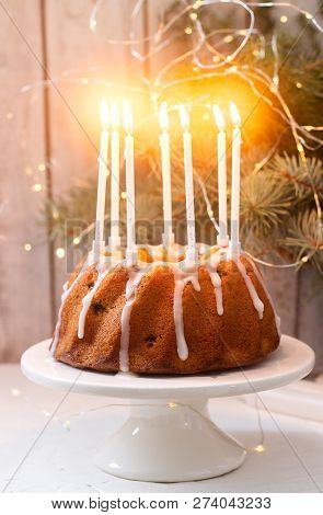 Pie With Raisins And Icing From Powdered Sugar On The Background Of Fir Branches And Garlands. Rusti