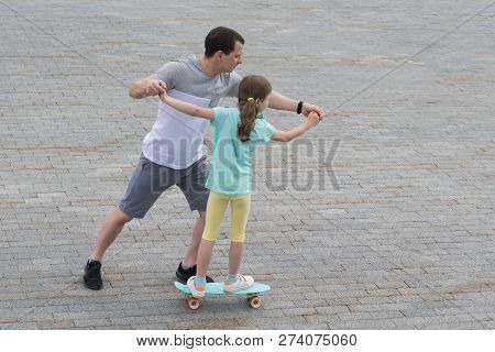 Dad Teaches Daughter To Skateboard In A City Park