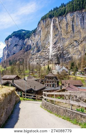 Sunny Summer View Of Amazing Touristic Alpine Village With Famous Church And Staubbach Waterfall, La