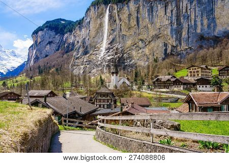 Sunny Summer View Of Amazing Touristic Alpine Village With Famous Church And Staubbach Waterfall, La