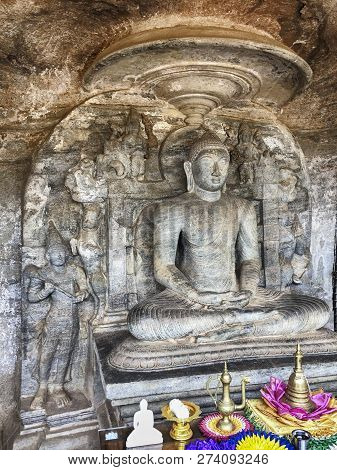 A Statue Of Buddha Carved Into A Stone Cliff Sits In A Lotus Pose In The Gal Vihare Rock Shrine In T