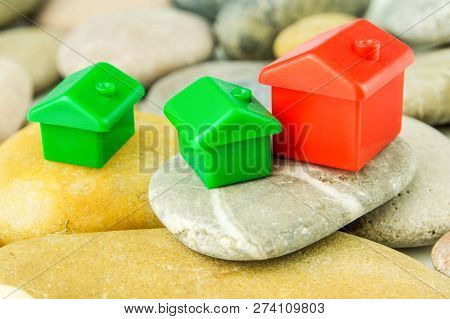 Three Little Green And Red Houses Made Of Plastic Are Laying On Bunch Of Grey Pebblestones