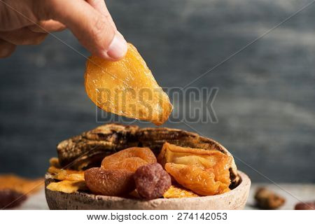 closeup of a young caucasian man taking a piece of dried pear from a rustic earthenware bowl full of an assortment of dried fruit, such as pear, peach, banana, strawberry, apple or apricot