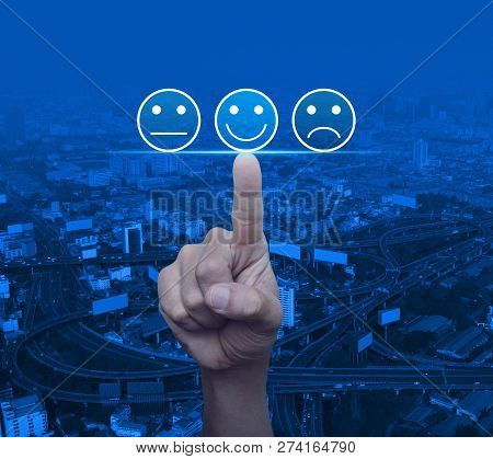 Hand Pressing Excellent Smiley Face Rating Icon Over Modern City Tower, Street, Expressway And Skysc