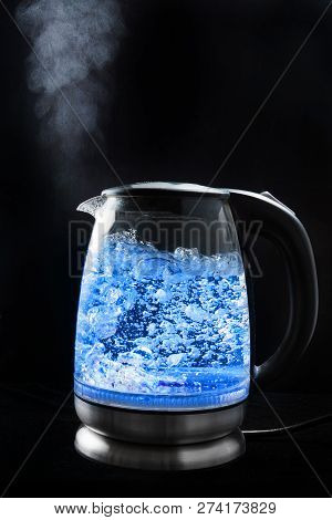 Boiling Glass Kettle With Blue Light On A Black Background, Steam Comes From The Spout