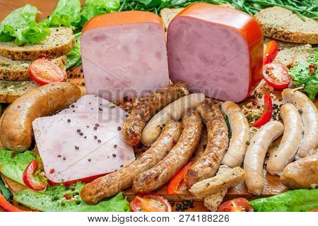 Assortment Of Meat Products Including Ham And Sausages With Greenary And Spices On Wooden Table Clos