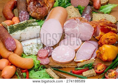 Assortment Of Meat Products Including Ham And Sausages With Greenary And Spices On Wooden Table Clos