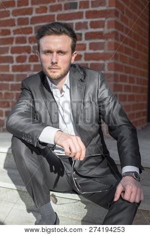 Half Length Portrait Of Young Sniling Man In Suit Sitting On Steps Outside Of His Office Building, P