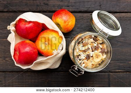 Homemade Granola In Glass Jar And Apples In Reusable Fabric Bag On Dark Wooden Table With Texture. H