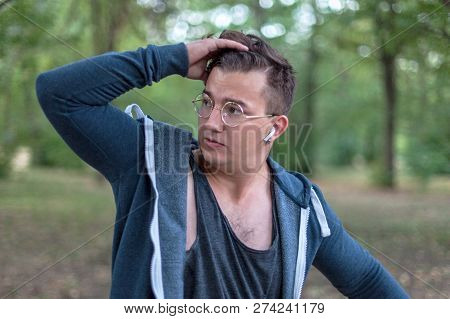Attractive Young Caucasian Man With Golden Round Glasses Touches His Dark Hair. Serious Expression, 