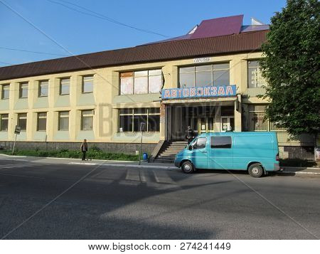 Ukraine, Khust - May 1, 2018: Poor Old Building Bus Station In Khust. Blue Van Stands On City Street