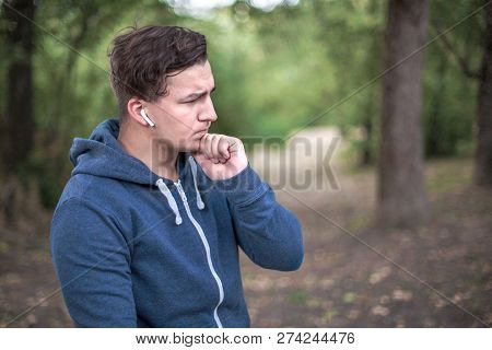 Young Handsome Causacian Man Stands At The Park, Outdoors, Touching His Chin, Thoughtful And Serious