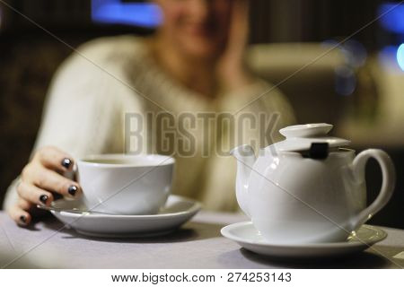 Teapot With A Cup Of Tea And Against The Background Of An Indistinct Silhouette Of The Girl