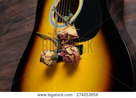 Acoustic Guitar With Dried Roses On The Wooden Table. Template For Advertising A Concert Of Memory W