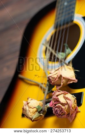Acoustic Guitar With Dried Roses On The Wooden Table. Template For Advertising A Concert Of Memory W