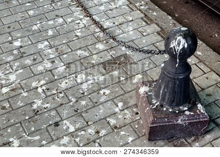 Black Bollard With A Chain On A Pedestrian Pavement Dirty In Bird Droppings, Paving Slabs In Bird Sh