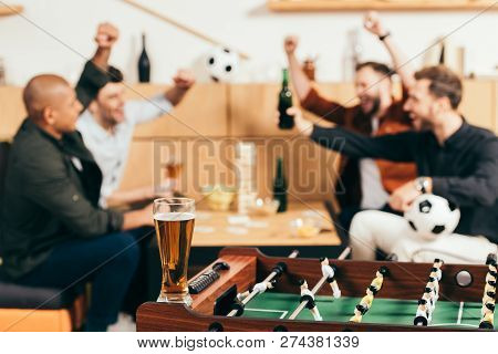 Selective Focus Of Happy Multicultural Friends Gesturing While Sitting At Tabletop With Beer And Sna