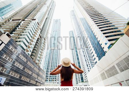 Back View Of Young Woman In Red Summer Dress Holding With Both Hands Straw Hat Looking Up On Skycrap