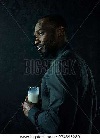 Healthy Young African Man Holging Cup Of Milk On A Bllack Studio Background.