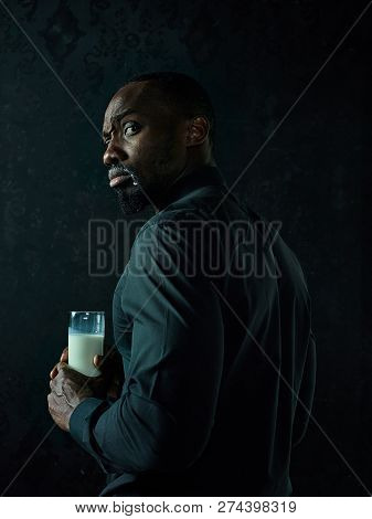 Healthy Young African Man Holging Cup Of Milk On A Bllack Studio Background.