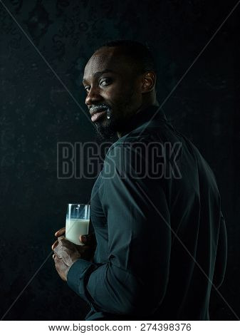 Healthy Young African Man Holging Cup Of Milk On A Bllack Studio Background.