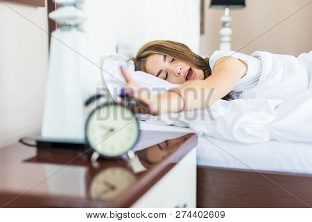 Sleepy Young Woman Stretching Hand To Ringing Alarm To Turn It Off. Early Wake Up, Not Getting Enoug
