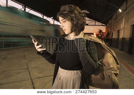 Young Teenager Woman With Backpack Alone At Train Station Checking Mobile Phone At Evening Light.