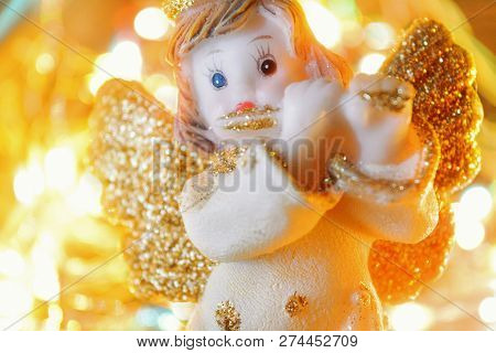 Figurine Of Little Angel With Golden Shiny Wings And Halo That Plays Flute On Shining Background Of 