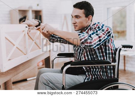 Young Man On Wheelchair Assembling Wooden Bookshelf At Home. Wooden Bookcase. Selfmade Furniture. Wh