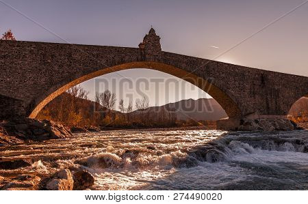 Landscape Of A Medieval Bridge Over A Turbulent River At Sunset