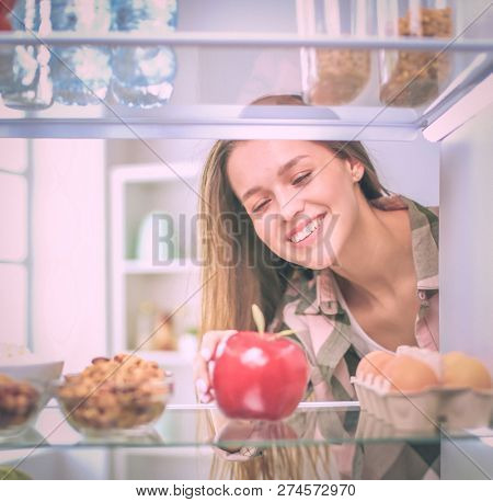 Portrait of female standing near open fridge full of healthy food, vegetables and fruits. Portrait of female