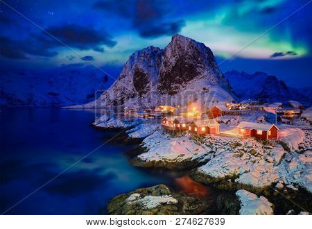 Famous tourist attraction Hamnoy fishing village on Lofoten Islands, Norway with red rorbu houses in winter snow illuminated in the evening with Aurora Borealis