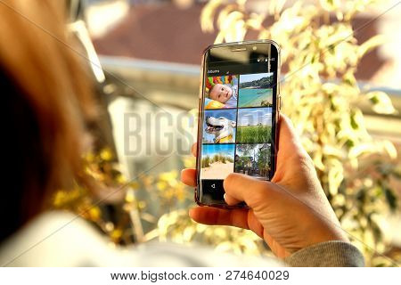 Smartphone With Album Photo Gallery On Screen. Photographs Thumbnails Of A Baby, A Dog And Some Land