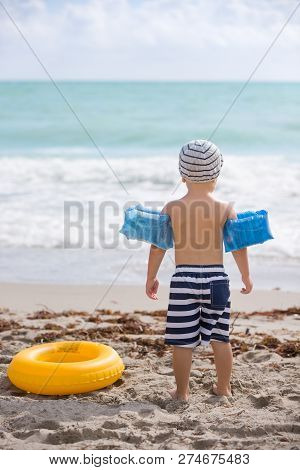 Back View On Cute Toddler Boy Wearing Safety Inflatable Armbands Standing On The Beach Ready To Jump