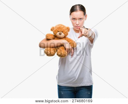 Young caucasian woman holding teddy bear over isolated background pointing with finger to the camera and to you, hand sign, positive and confident gesture from the front