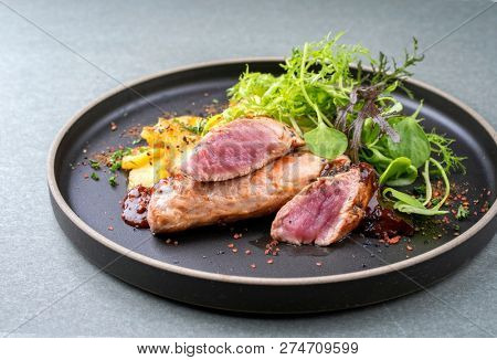 Fried suckling pig fillet with potatoes and lettuce offered as closeup in a modern design plate with spicy sauce