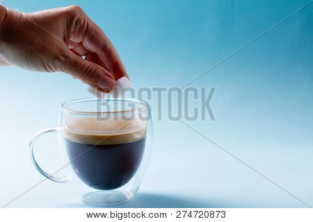 Hand Holding Cubes Of Sugar Over Cup Of Coffee Over Blue Background