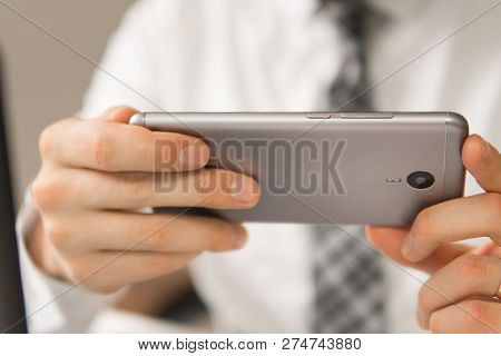 Young Bearded Businessman. Light Background. Holding Smartphone In Hand. Inancial Business. Office W