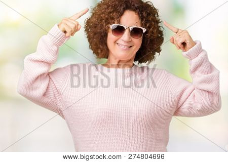 Beautiful middle ager senior woman wearing pink sweater and sunglasses over isolated background Smiling pointing to head with both hands finger, great idea or thought, good memory
