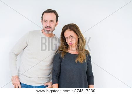 Beautiful middle age couple in love over isolated background puffing cheeks with funny face. Mouth inflated with air, crazy expression.